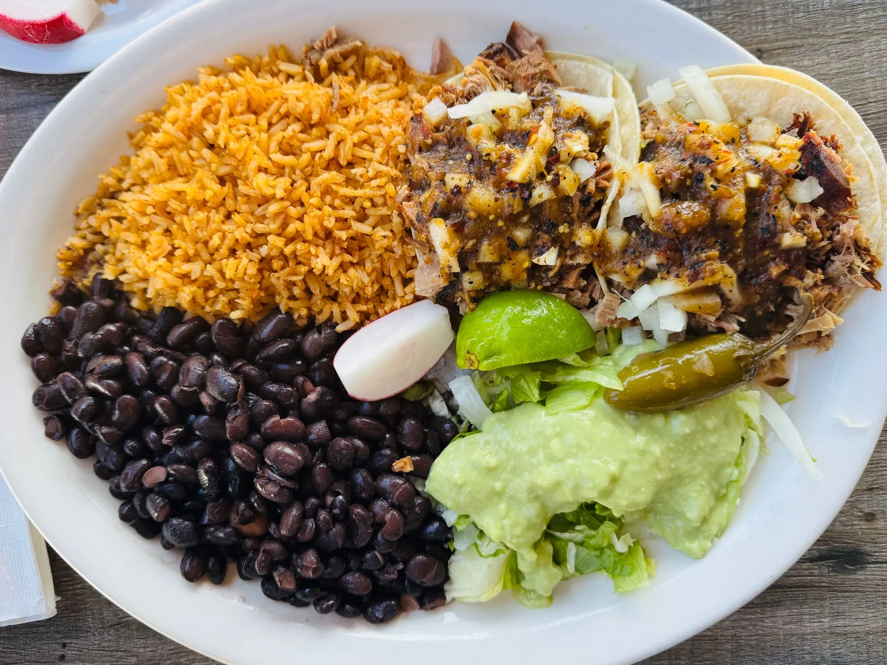 Two carnitas tacos with salsa verde, rice, and black beans